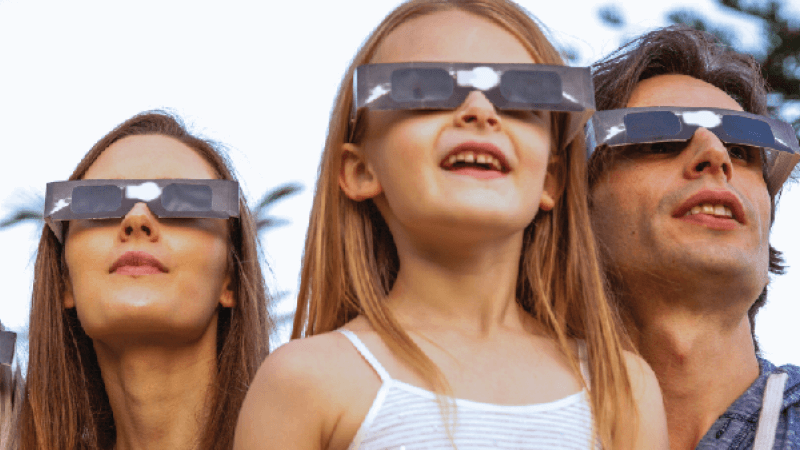 A young girl with her parents wear eclipse glasses while viewing the sun