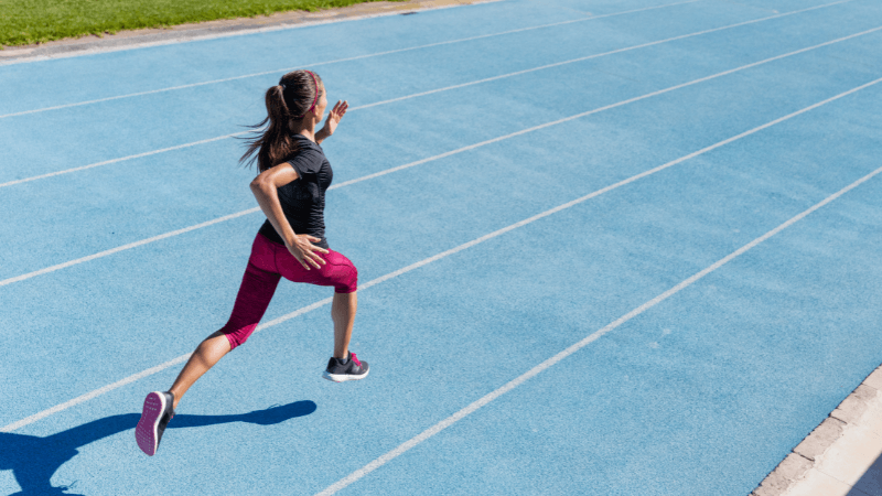 A person with a ponytail running on a blue track