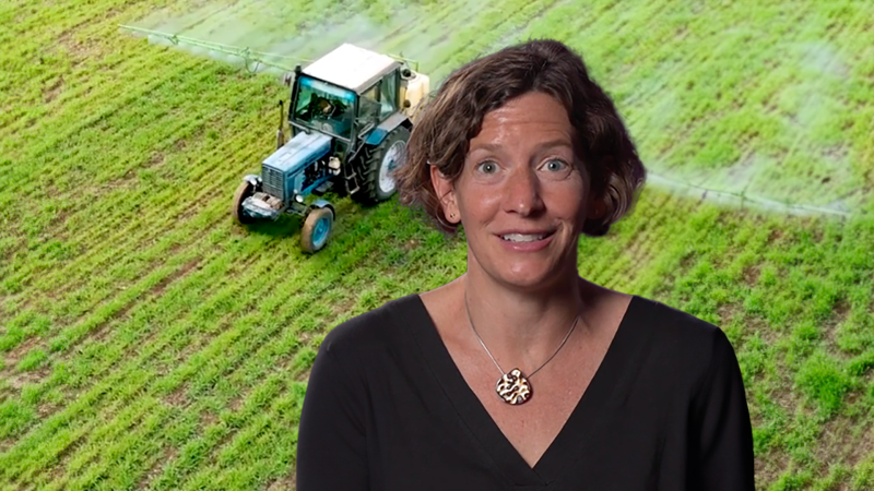 Nicola Twilley smiling in front of a field being farmed by a tractor.