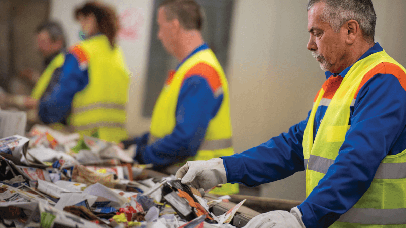 A man manually sorts recyclables on a conveyer belt