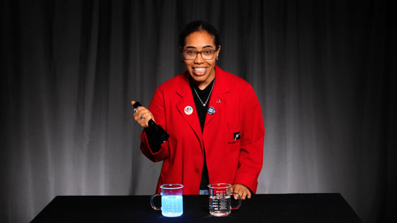 Museum Educator Morgan with a beaker of glowing tonic water 