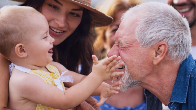 A baby reaches for the face of an older man.