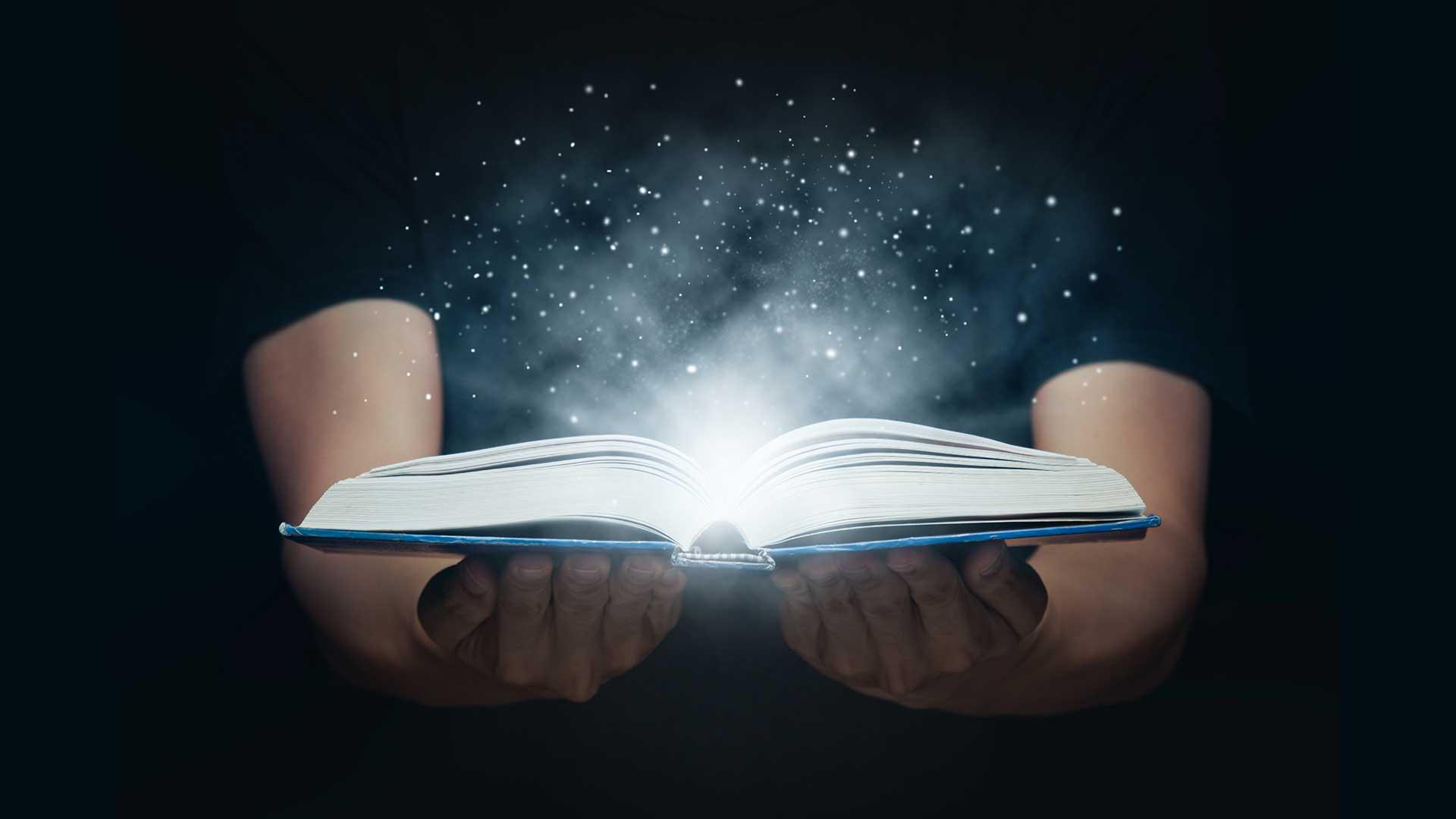 A person holding a book with light coming from the pages.