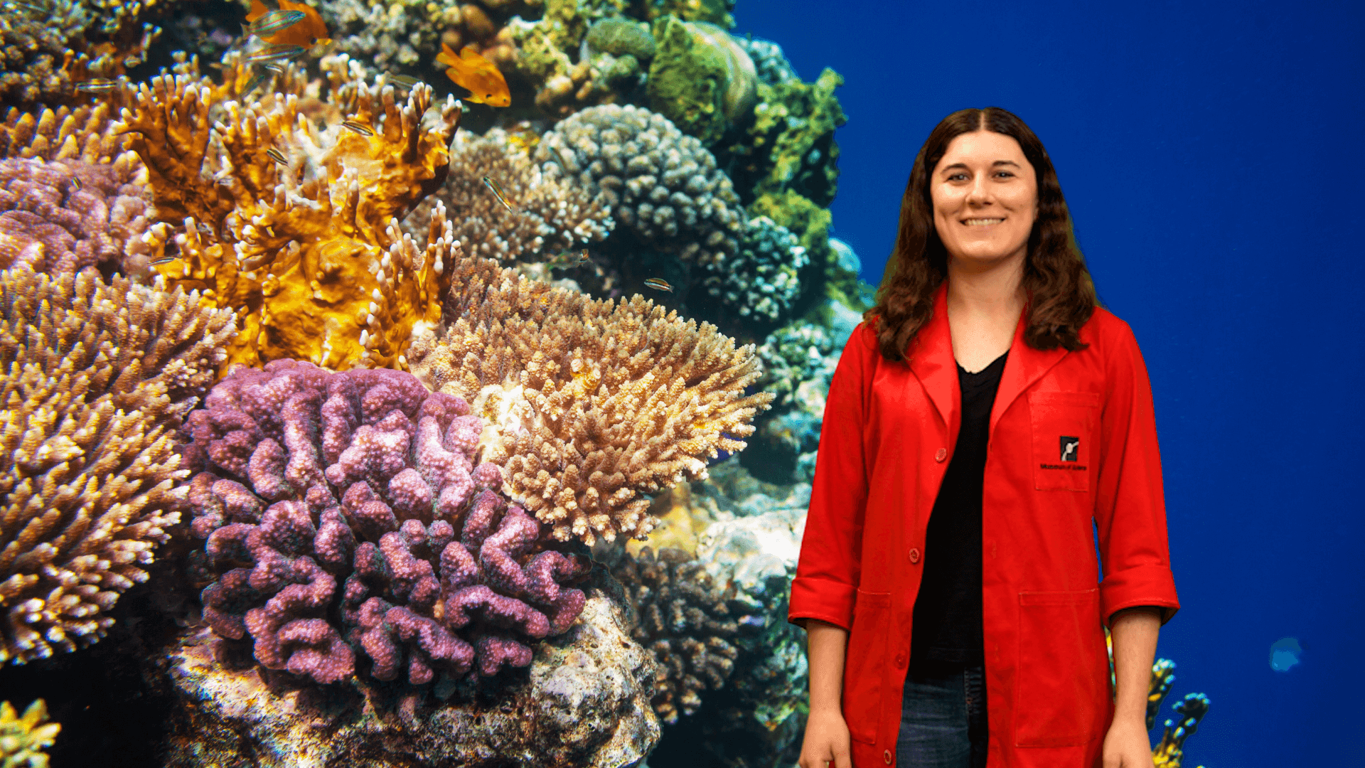 Museum Educator in a red lab coat standing next to coral