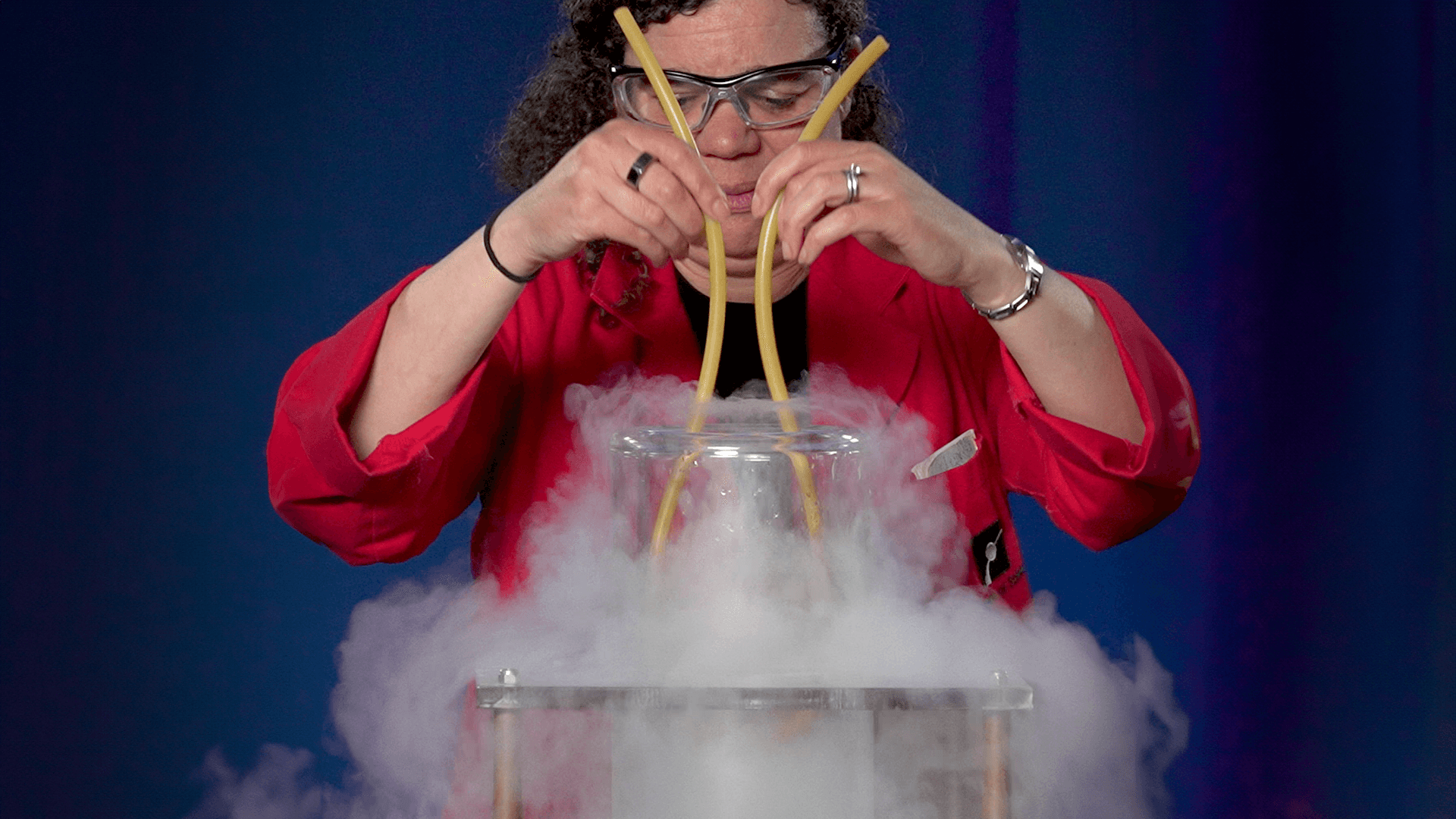 Museum Jeannine in a red lab coat putting a rubber tube in a bucket of liquid nitrogen