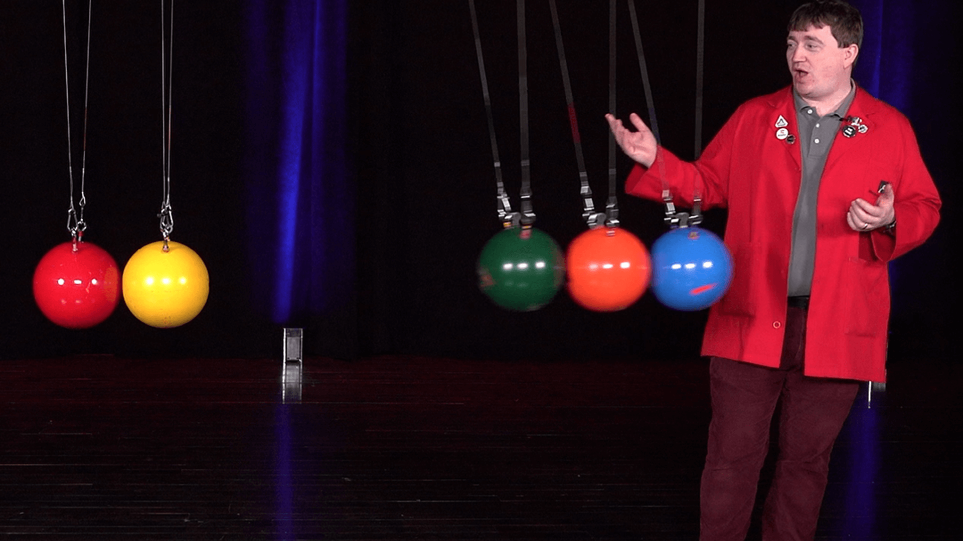 Museum Educator Eric standing next to a Newton's Cradle of bowling balls