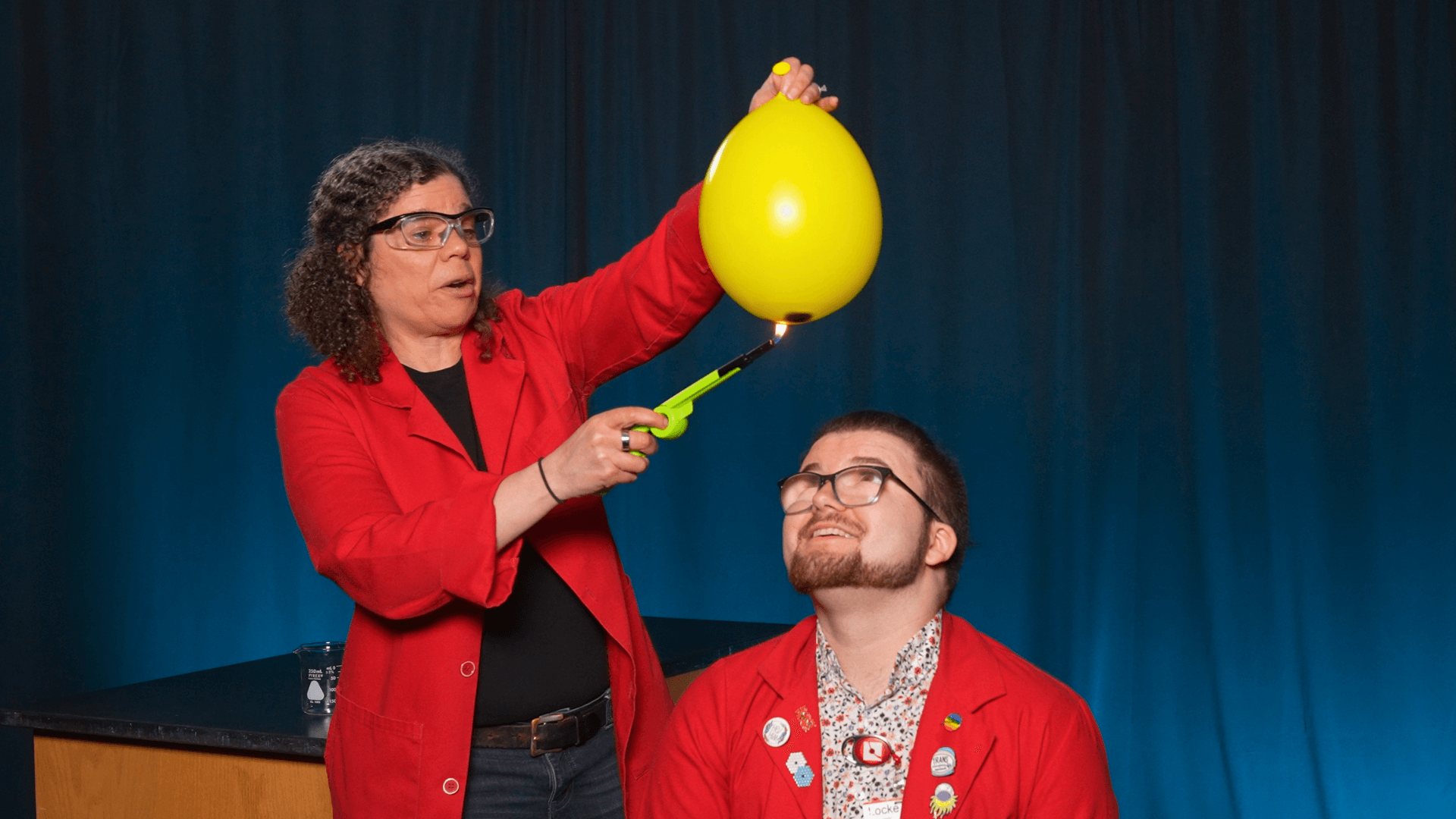 Jeannine holds a balloon filled with water over Locke's head while trying to pop it with fire