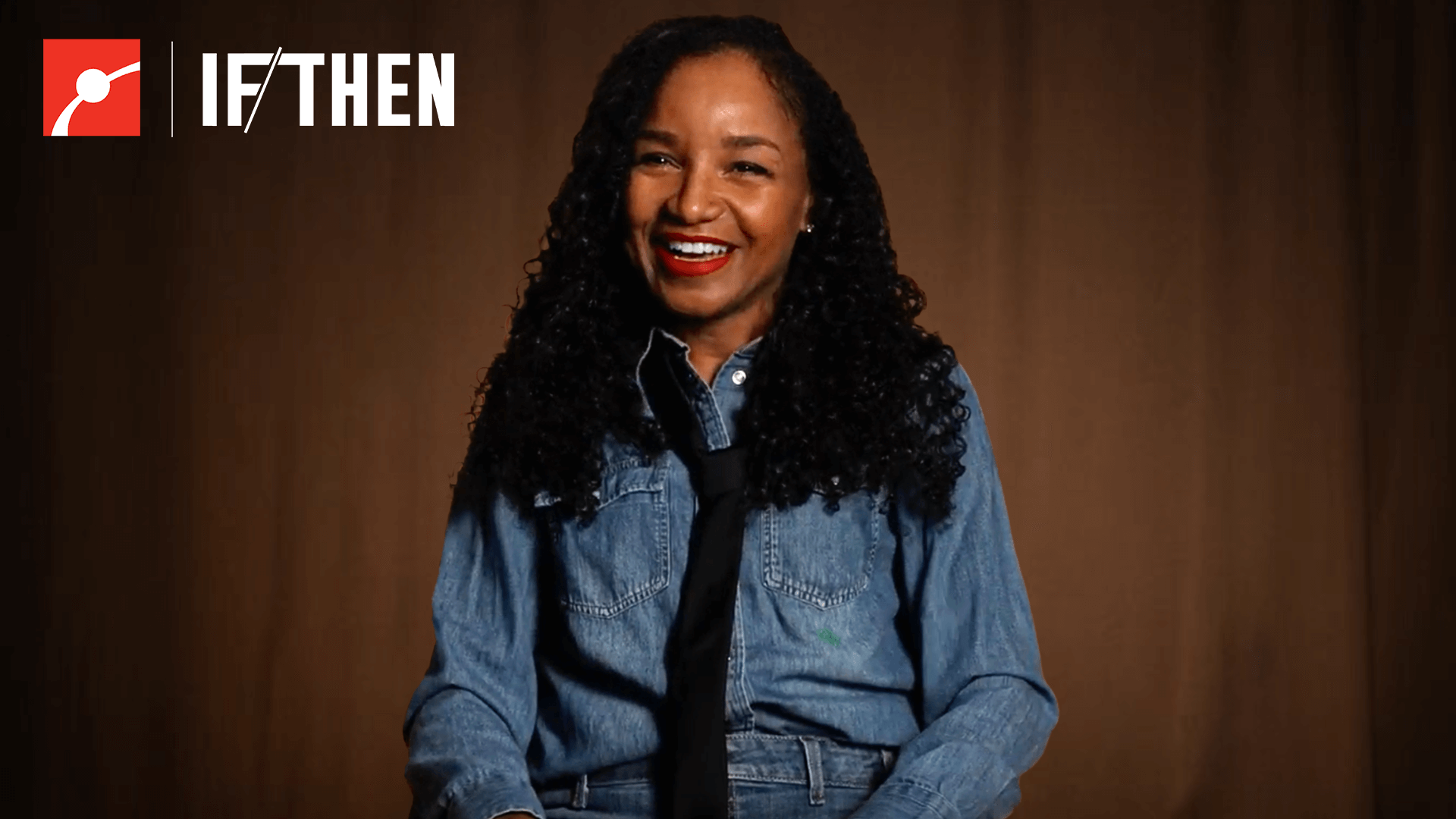 Renee Gosline smiling in front of an orange lit dark curtain.