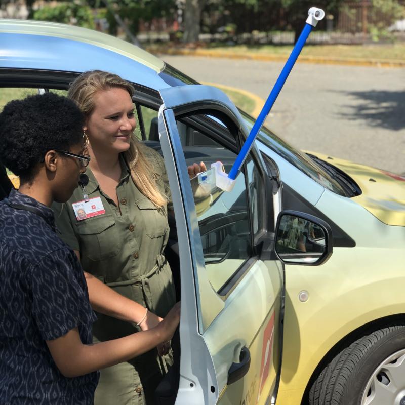 Two individuals examining a temperature sensor attached to a car.