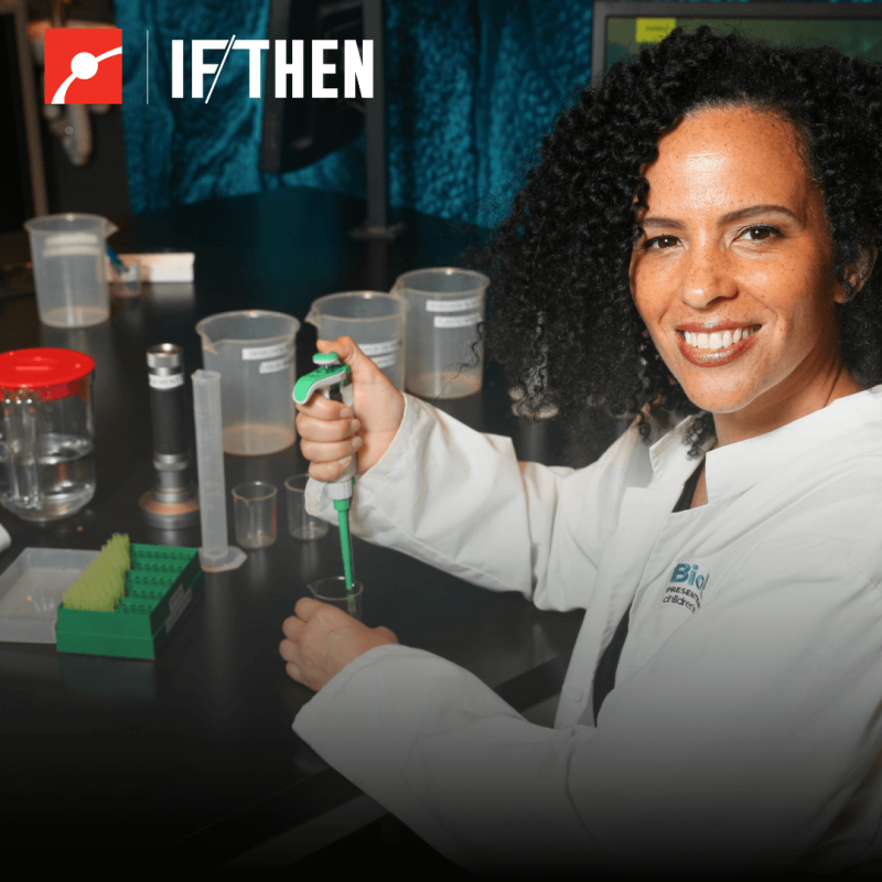 Raychelle Burkes pipettes at a bench while smiling at the viewer